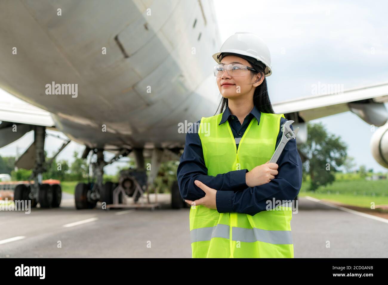 Asiatische Frau Ingenieur Wartung Flugzeug Arm gekreuzt und hält Schraubenschlüssel vor Flugzeug von Reparaturen, Fixes, Modernisierung und Renovierung in Flughafen Stockfoto