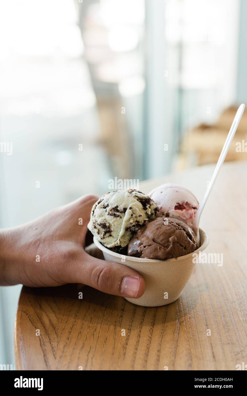Mann hält eine Tasse Schokolade, Erdbeere und Minze Schokolade Chip Eis auf einem Holztisch Stockfoto