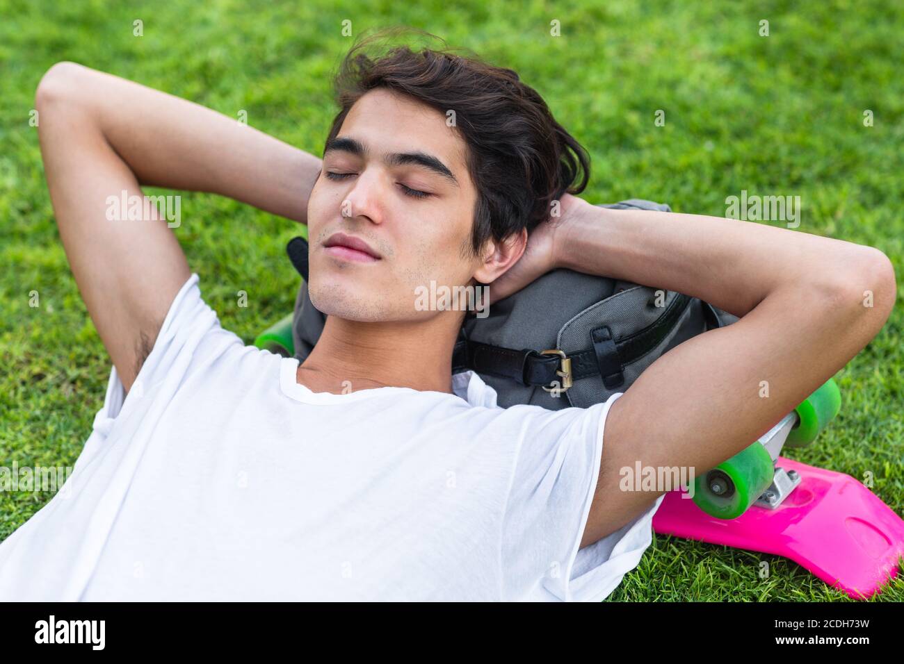 Nahaufnahme eines entspannten jungen Mannes, der im Sommer auf dem Rasen in einem Outdoor-Park schläft. Stockfoto