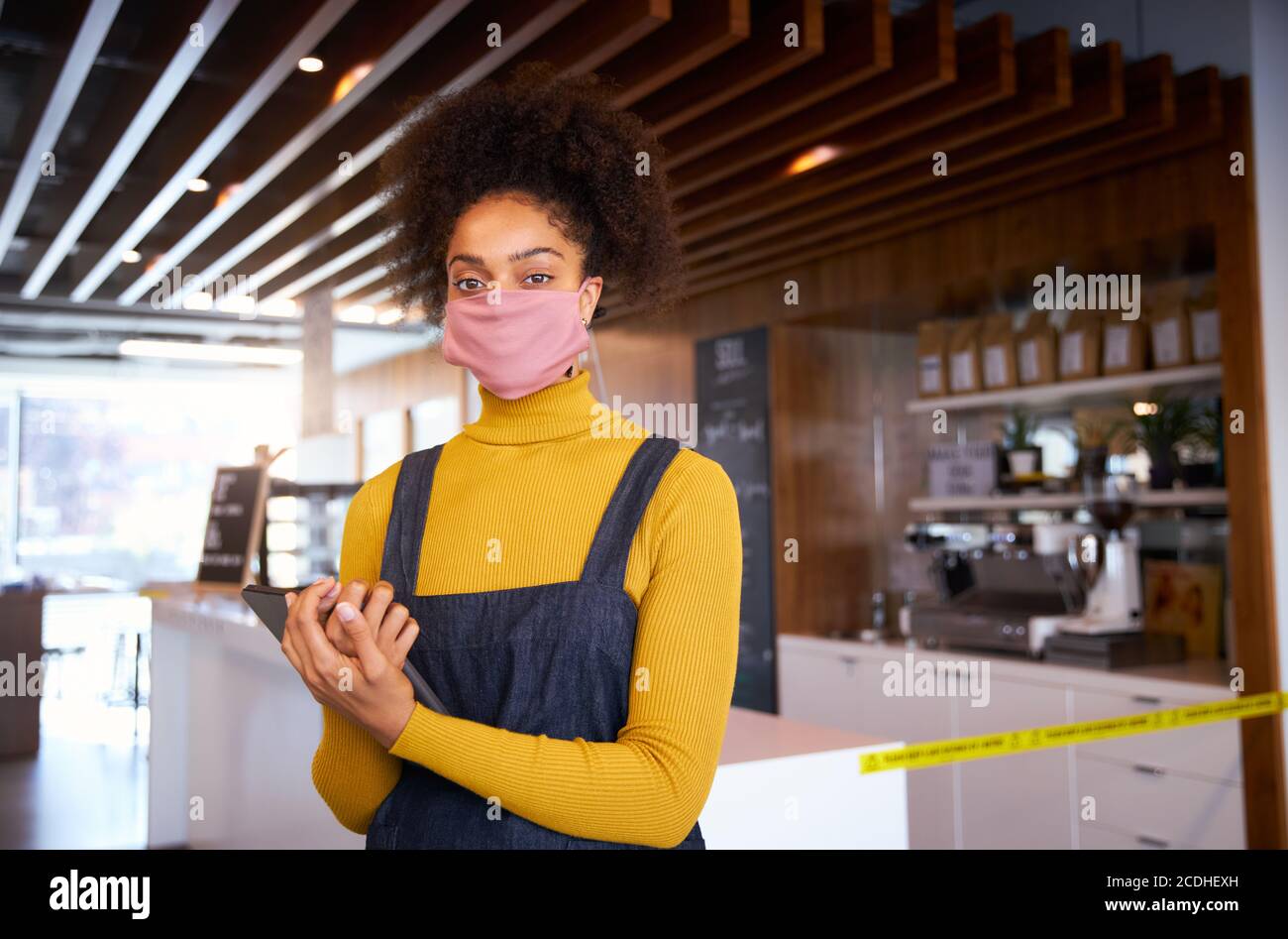 Weibliche afrikanische Café-Besitzer trägt Gesichtsmaske stehen vor der Theke mit digitalen Tablet. Stockfoto