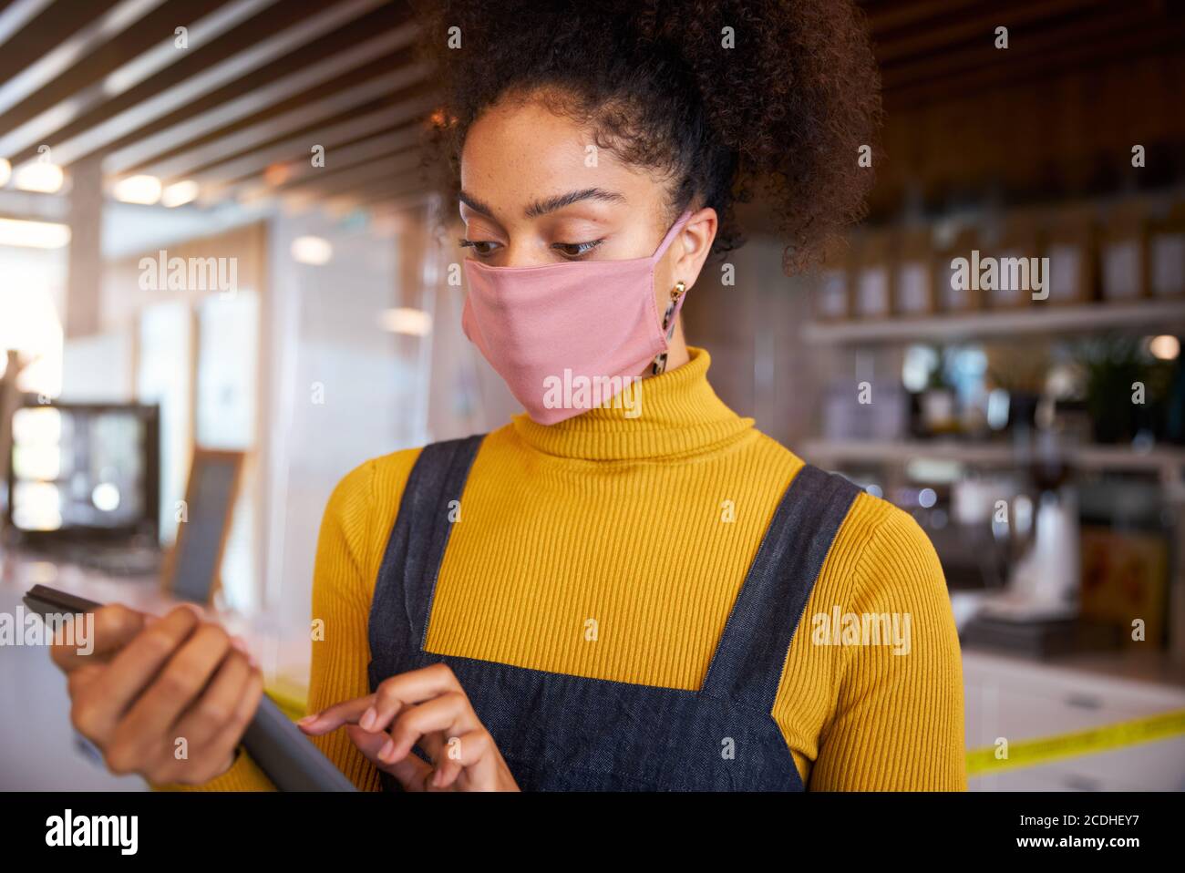 Weibliche afrikanische Café-Besitzer trägt Gesichtsmaske stehen vor der Theke Durchführung Stock Check. Stockfoto