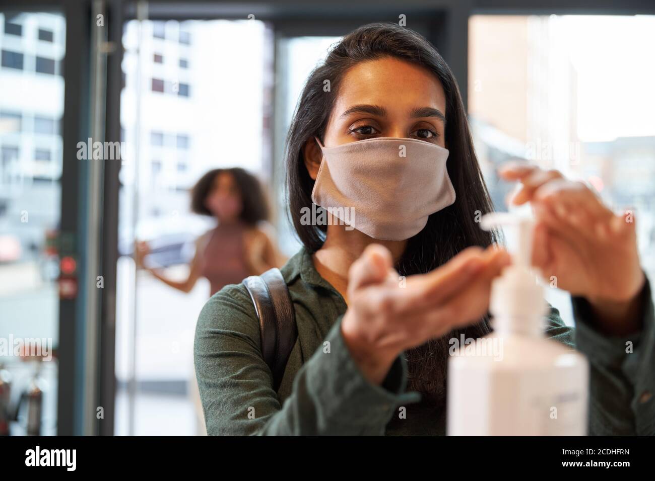 Geschäftsfrau, die Handgel verwendet, bevor sie das Büro an der Rezeption betritt Stockfoto