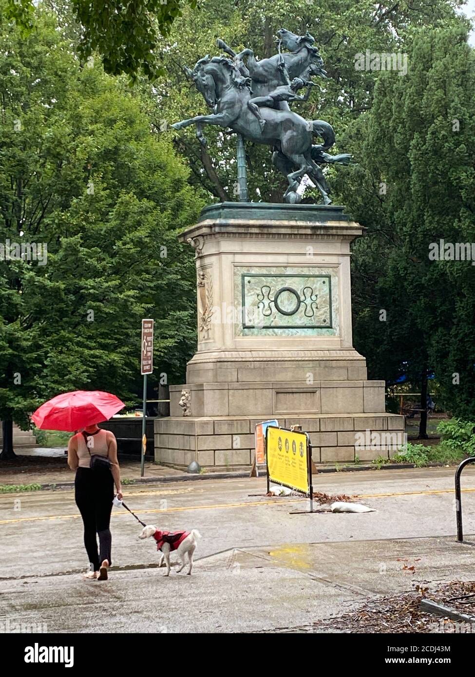 Frau geht allein an einem regnerischen Tag mit ihrem Hund am Südeingang des Prospect Park, Brooklyn, New York. Stockfoto