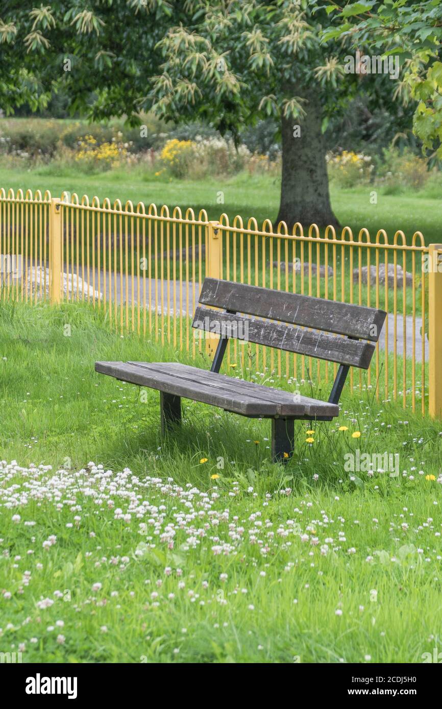 Überwucherter, einsamer öffentlicher Sitz/Bank auf einem Kinderspielplatz, der während der britischen Covid-Sperre von Menschen leer war. Verlassene öffentliche Räume, leere Parkbank in Großbritannien. Stockfoto