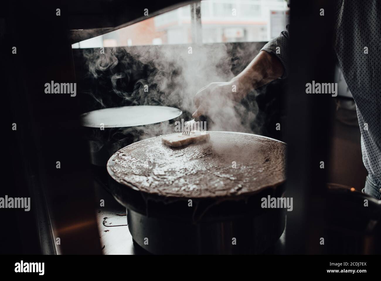 Hand des Küchenchefs, der beim Kochen im Restaurant heiße Crepes buttert Küche Stockfoto