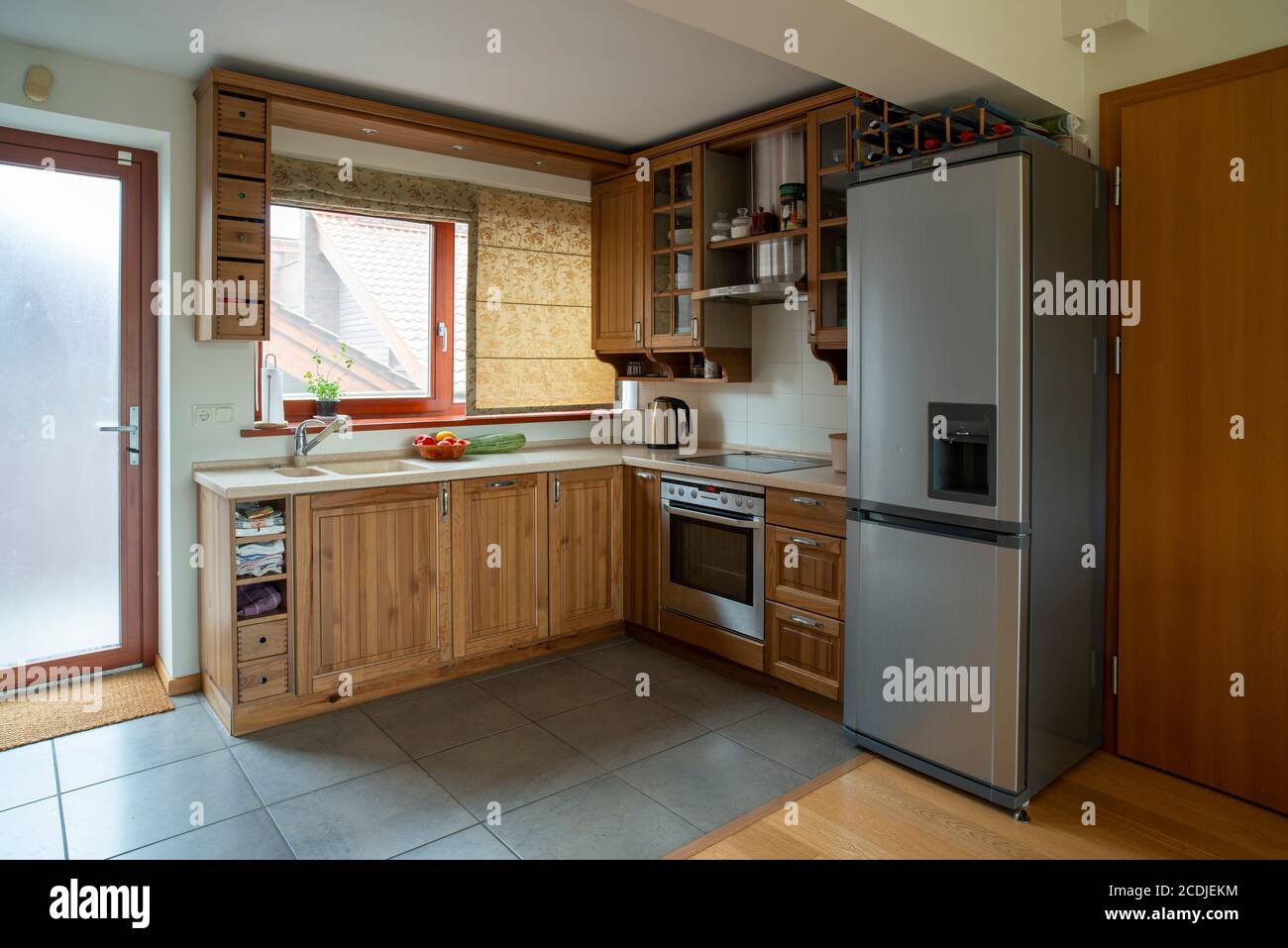 Eckküche mit Fenster in kleiner Wohnung. Holzmöbel in warmen Farbtönen, Weitwinkelansicht. Stockfoto