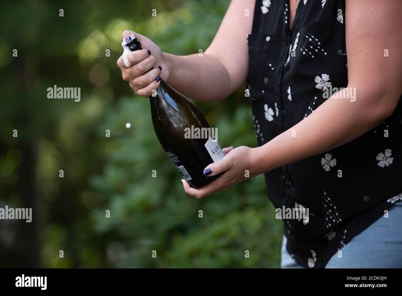 Eine Frau öffnet eine Flasche Champagner bei einem Abschlussfeier Stockfoto