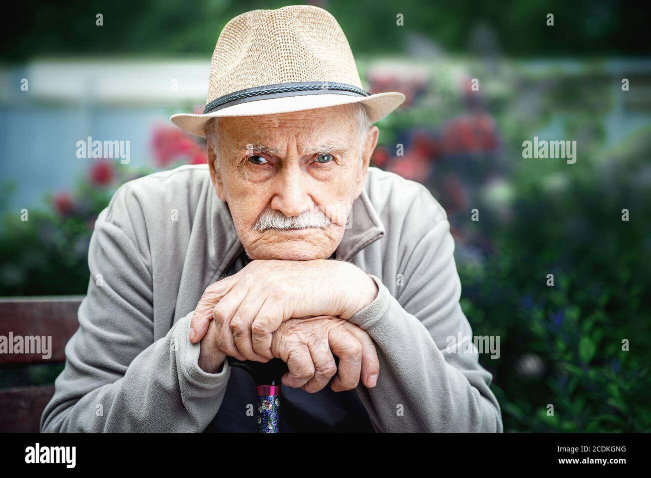 Trauriger, wütender alter Mann mit Hut sitzt in einem Freiluftgarten. Konzept von Einsamkeit und einsamem Alter Stockfoto
