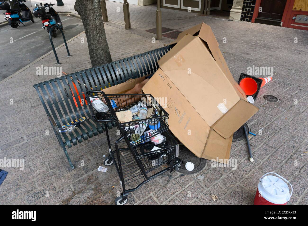 Eine obdachlose Person, mit Habseligkeiten in einem Einkaufswagen, schläft auf einer Metallbank unter Pappe bei 10th St. und Congress Ave. Früh am Morgen in der Innenstadt von Austin im August 2020. ©Bob Daemmrich Stockfoto
