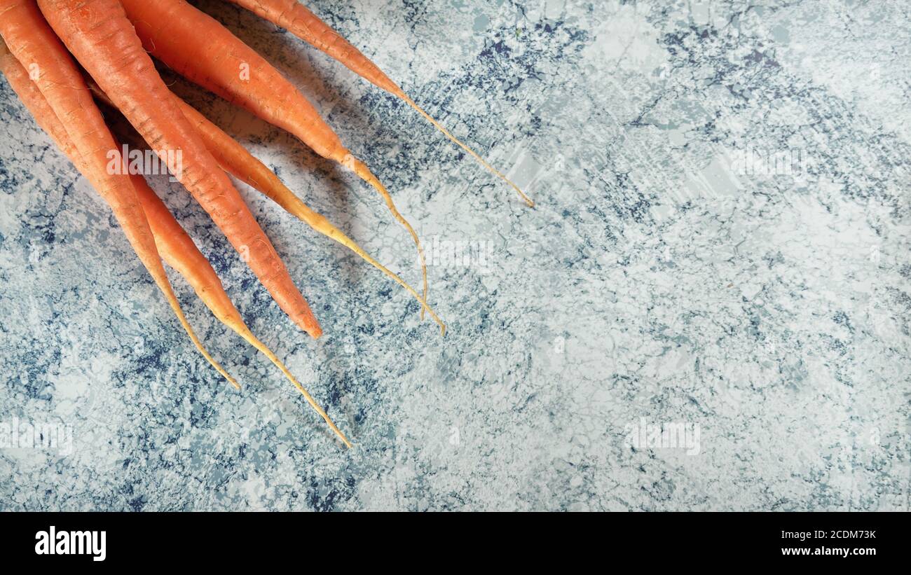 Frische Karottenwurzeln auf blauem Stein Marmor wie Brett, breites Banner mit Platz für Text rechts Stockfoto