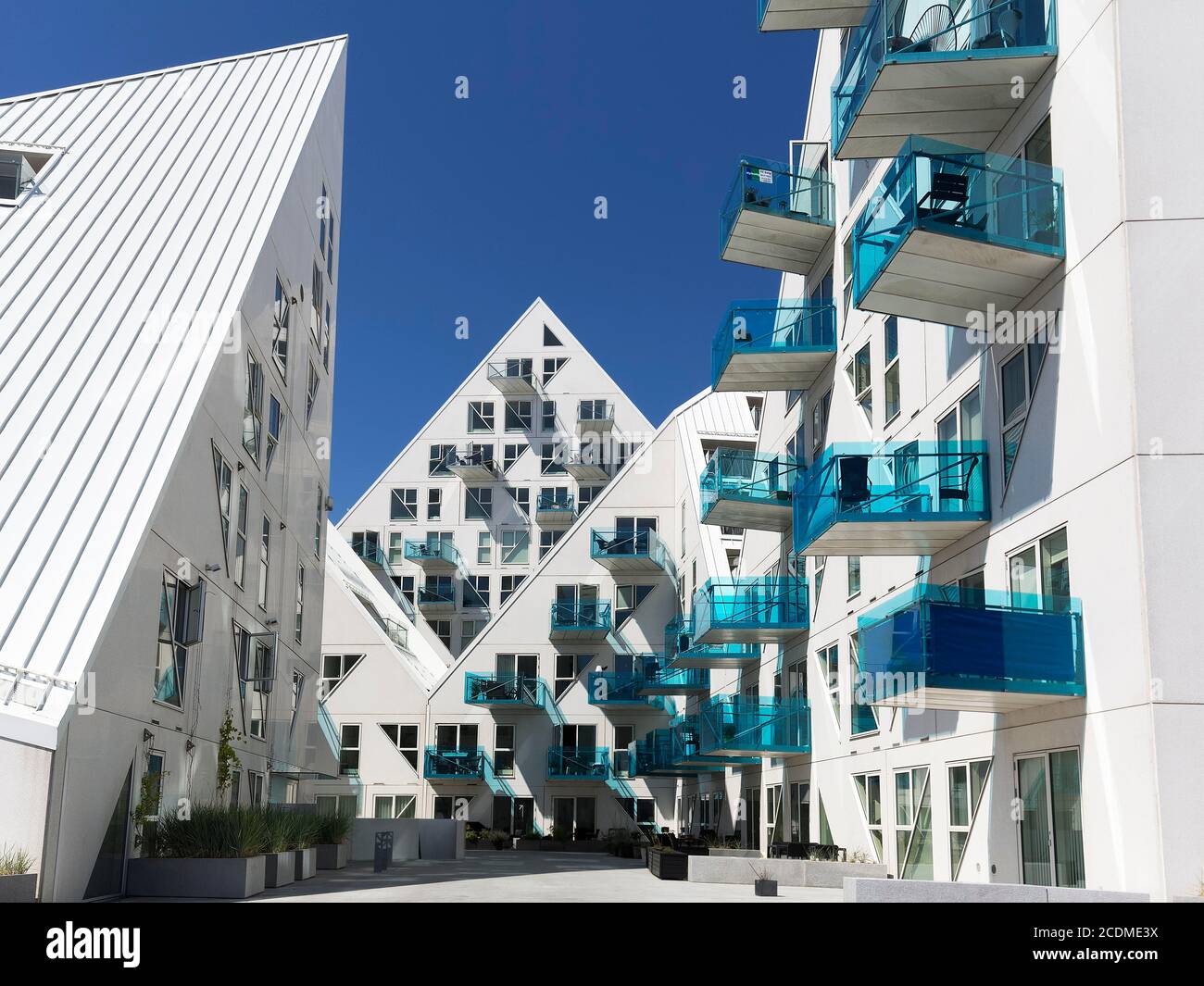 Weiße Wohnanlage mit türkisfarbenen Balkonen gegen einen blauen Himmel, pyramidenförmige Gebäudeskulptur Isbjerget, Eisberg, moderne Architektur in Stockfoto