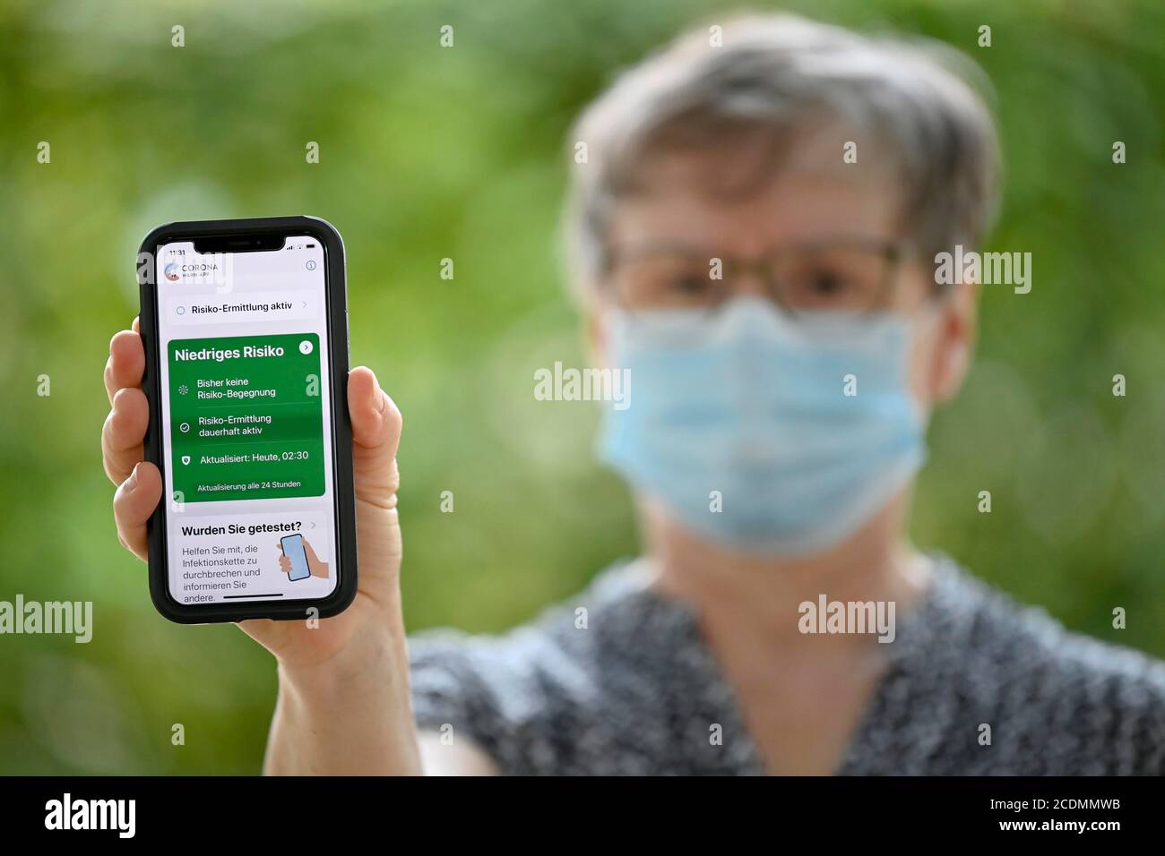 Ältere Frau mit Gesichtsmaske, zeigt Smartphone mit Corona Warn-APP in der Grünzone, Corona-Krise, Baden-Württemberg, Deutschland Stockfoto
