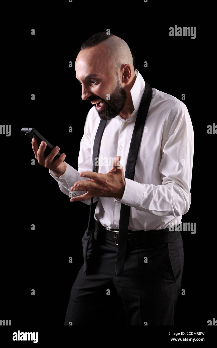 Porträt eines wütenden jungen hispanischen Mannes mit einer kreativen Frisur, verliert seine Temperament und wütend auf das Telefon schreien. Szene auf schwarzem Hintergrund. Stockfoto