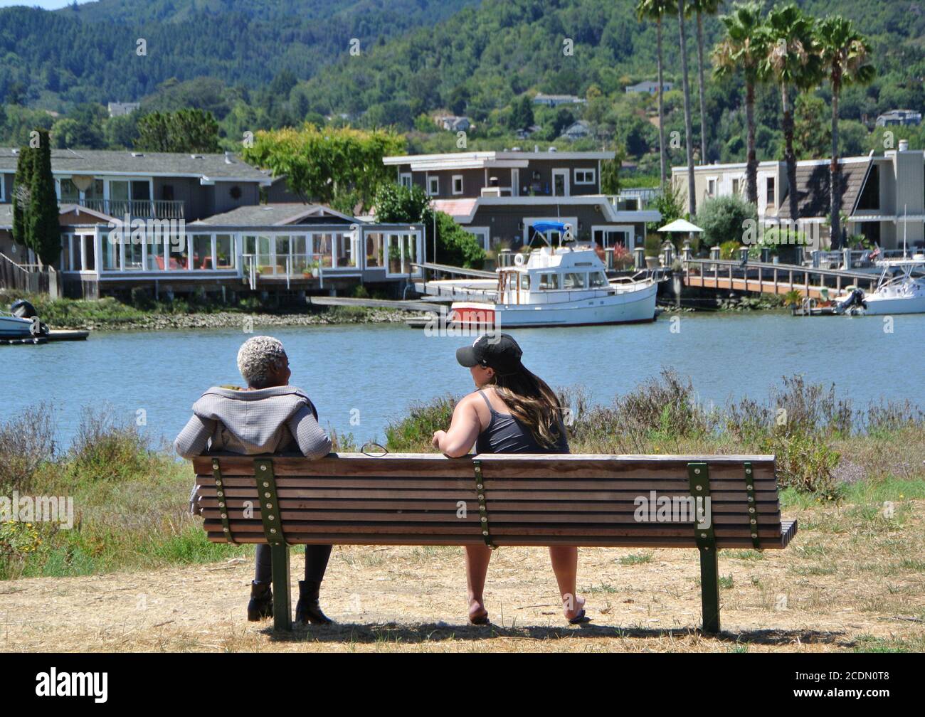 Zwei Freundinnen, eine schwarze und eine weiße, sprechen auf einer Bank während der covid 19 Beschränkungen in larkspur kalifornien Stockfoto