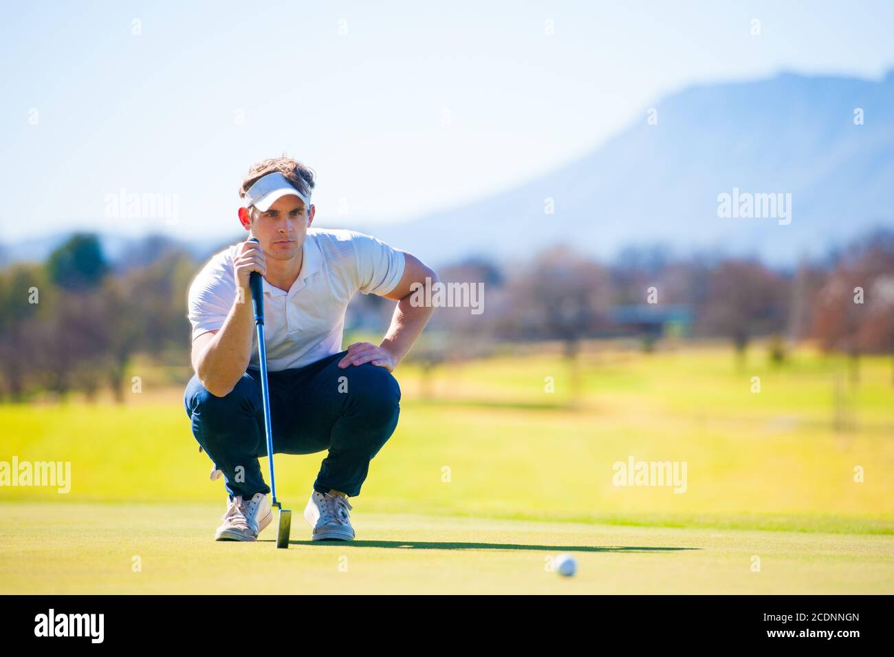Mitte der zwanziger Jahre männlichen Golfer Planung seiner Putting Schuss auf die PIN auf einem Grün an einem hellen sonnigen Tag Stockfoto