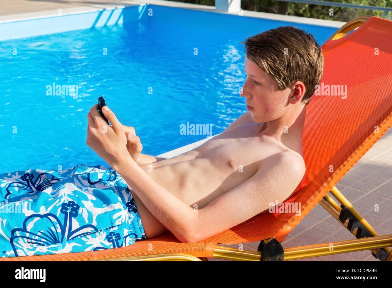 Jugendlicher, der am Swimmingpool ein Mobiltelefon betreibt Stockfoto