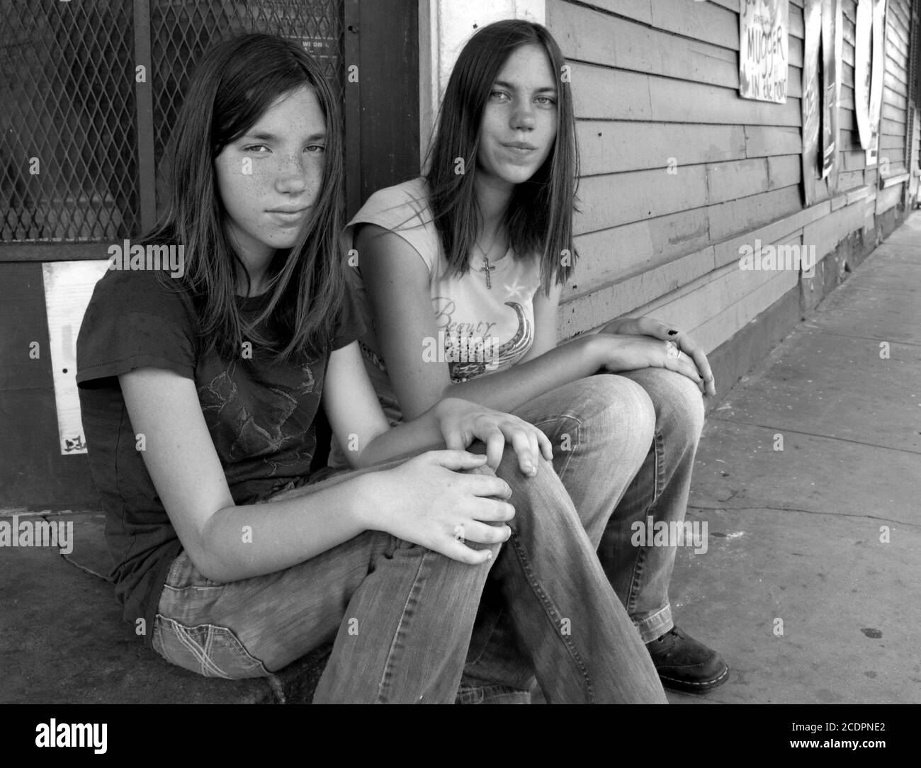 Ein schwarz-weißes Porträt von zwei jungen Teenagerschwestern, die am Bürgersteig in der Marigny-Bywater-Gegend von New Orleans, Louisiana, USA, sitzen. Stockfoto