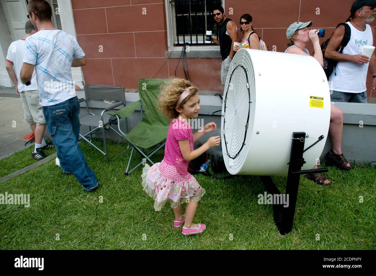 Ein junges Mädchen steht während einer Hitzewelle während eines Straßenfestivals in New Orleans, Louisiana, USA, vor einem großen Kühlventilator. Stockfoto