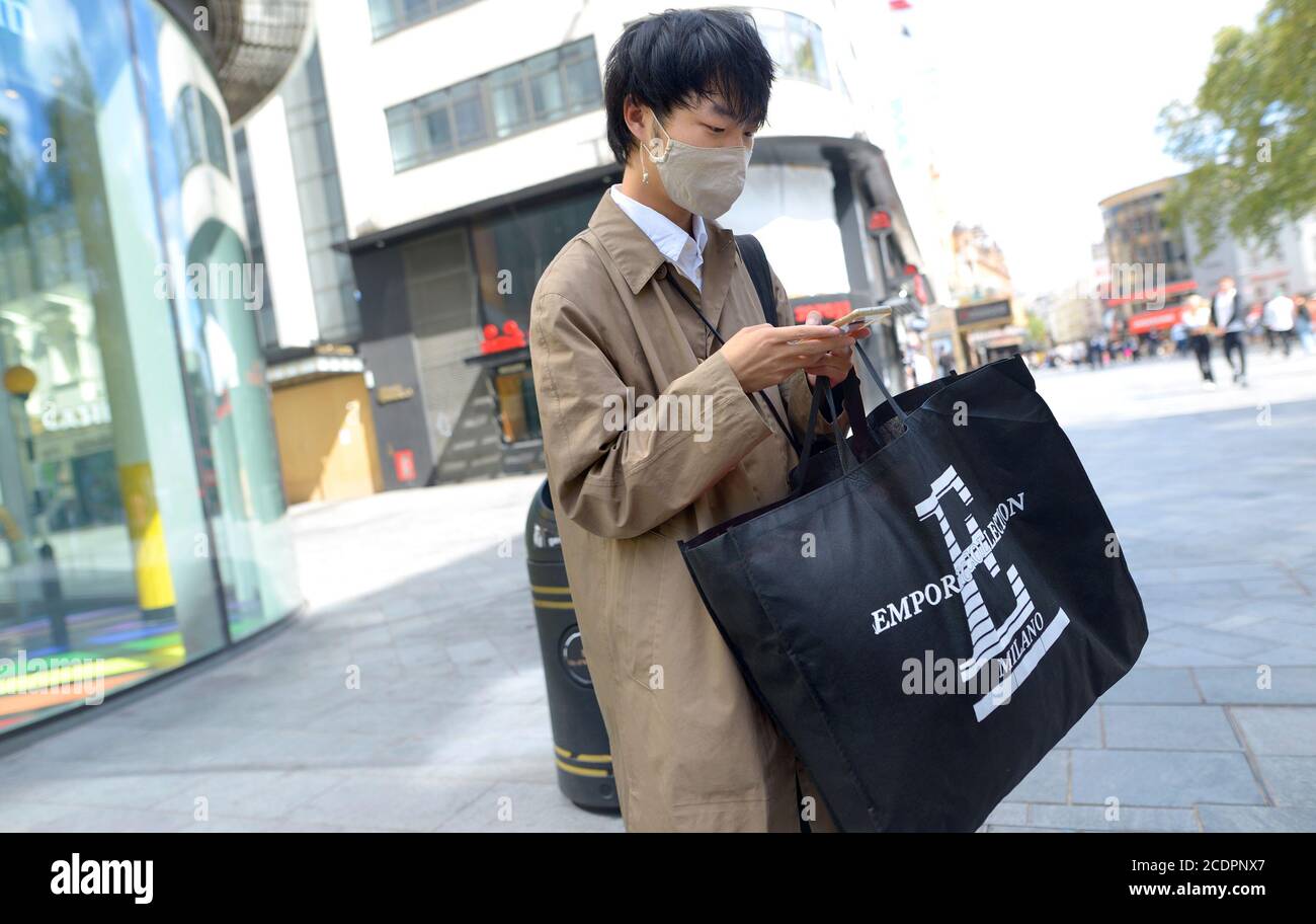London, England, Großbritannien. Japanischer Mann mit Einkaufen, trägt eine Gesichtsmaske und auf seinem Handy während der COVID Pandemie, August 2020 Stockfoto