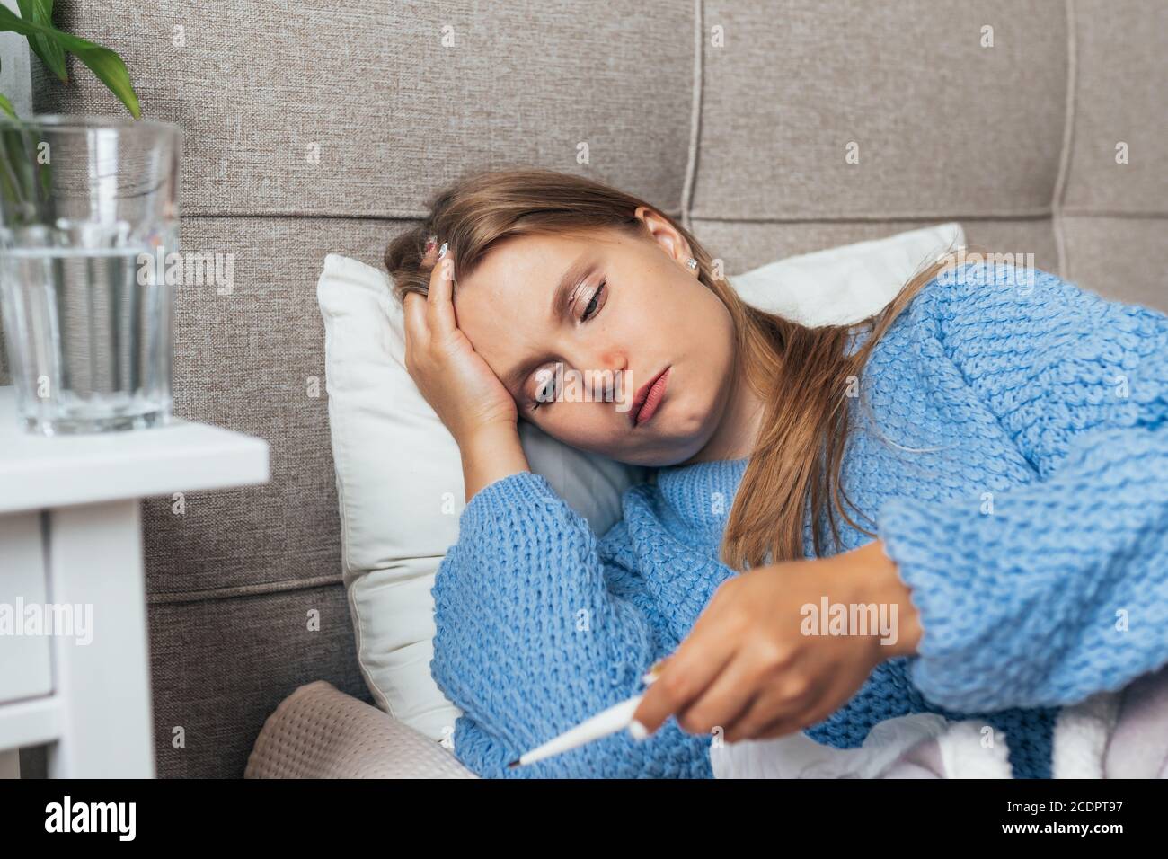 Kranke Frau liegt im Bett unter Decke und überprüfen Thermometer. Kopfschmerzen, Grippe, Erkältung, Virus. Stockfoto