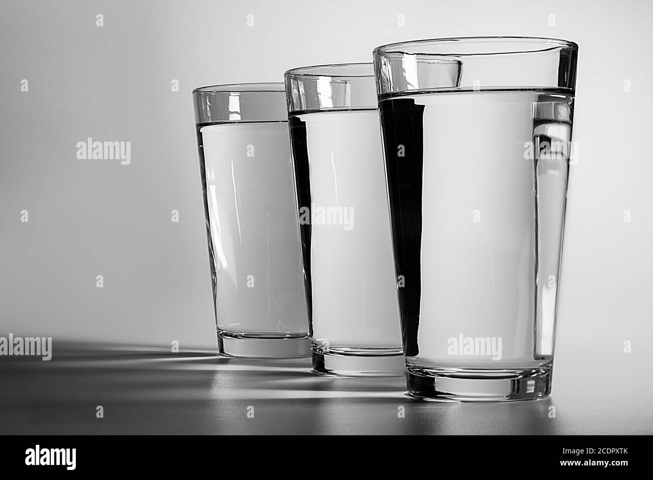 Drei Gläser Wasser auf einem schlichten weißen Hintergrund mit Schatten werfen sich über den Vordergrund Stockfoto