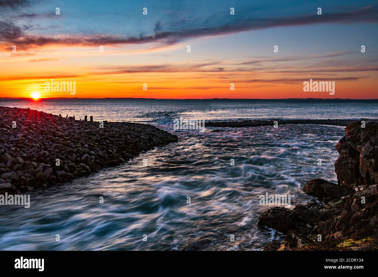 Fluss, der bei Ebbe im Sonnenuntergang ins Meer fließt Stockfoto