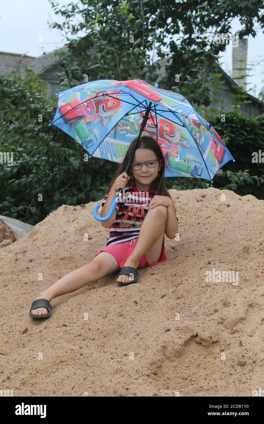 Mädchen unter einem hellen Regenschirm spielen unter Regen im Garten Im letzten Sommertag im Urlaub Stockfoto