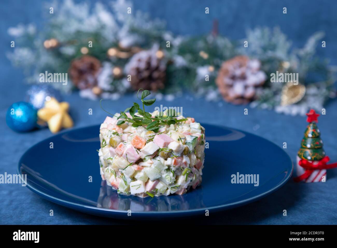 Olivier Salat auf einem blauen Teller, verziert mit Erbsensprossen. Traditioneller russischer Salat zu Neujahr und Weihnachten. Stockfoto