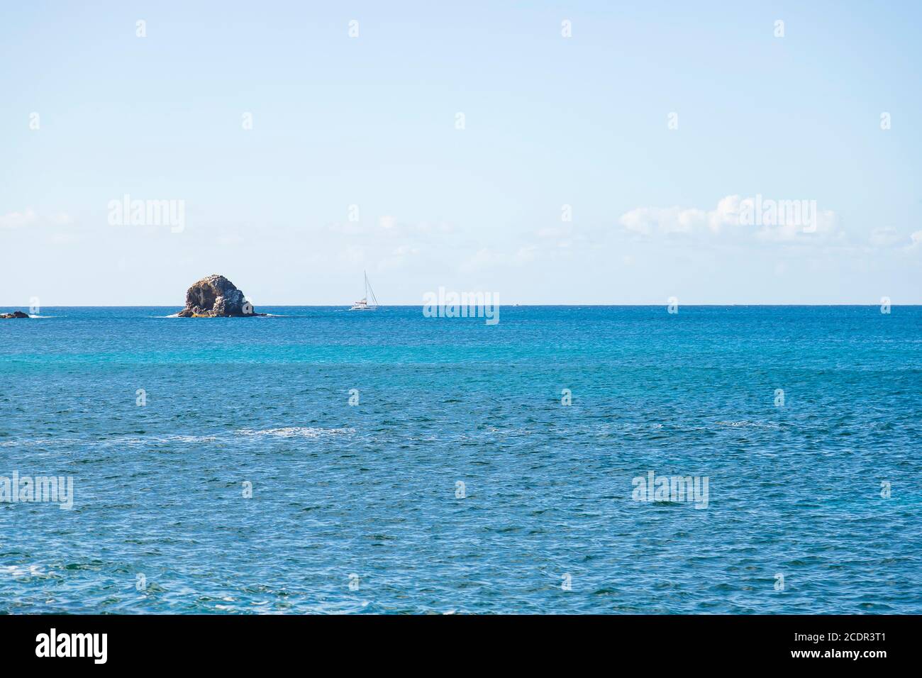 Eine im Meer isolierte ozeanische Landform mit einer einzigen yacht segelt vorbei im Hintergrund Stockfoto