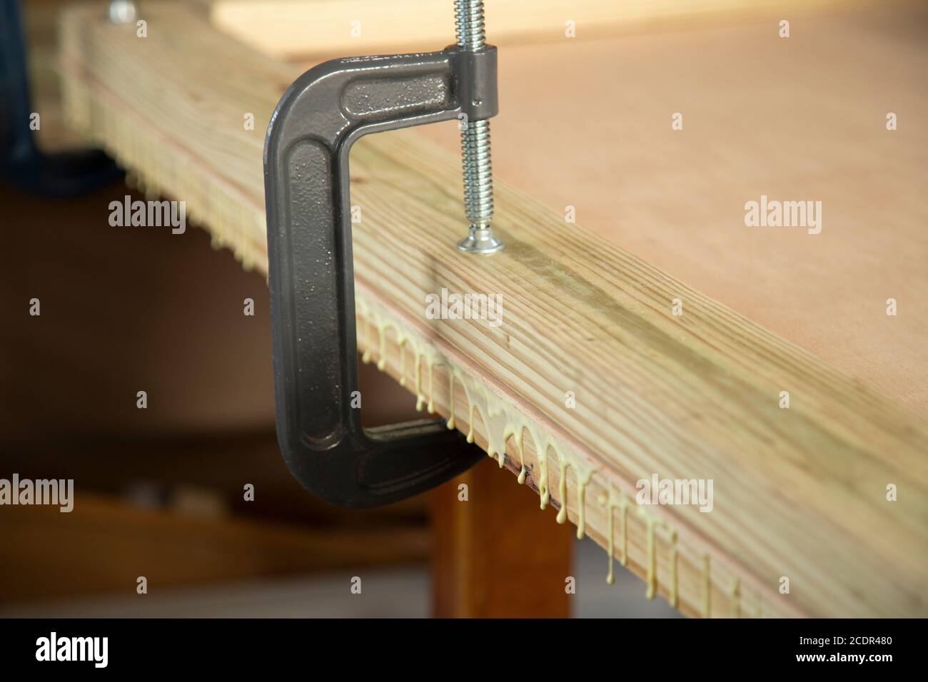 Eine G-Klemme, mit der das Vormaterial eines befestigt wird Bündige Tür zum Rahmen, wodurch überschüssiger Holzleim entsteht Greifen Sie heraus Stockfoto