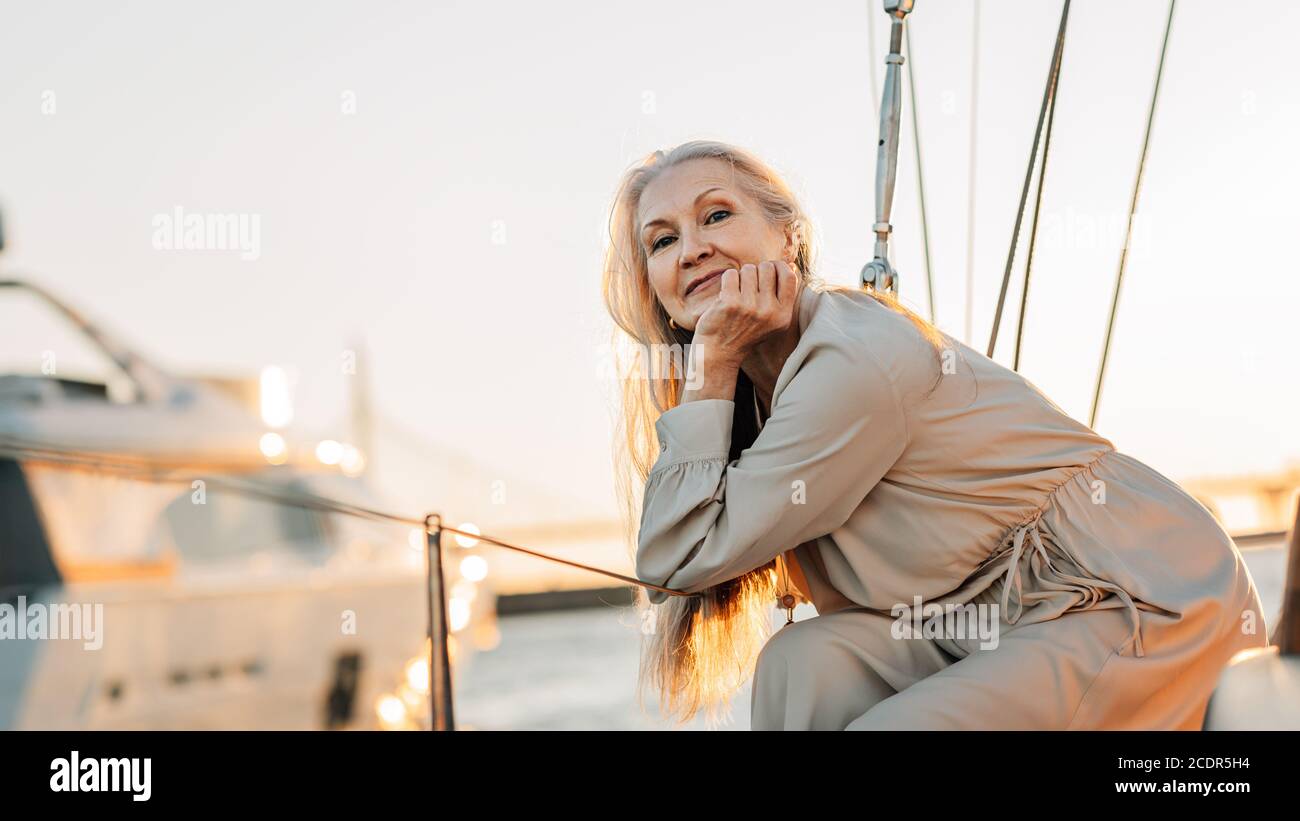 Porträt einer reifen kaukasischen Frau mit langen grauen Haaren Blick direkt auf die Kamera, während Sie auf einem Segelboot sitzen Sonnenuntergang Stockfoto