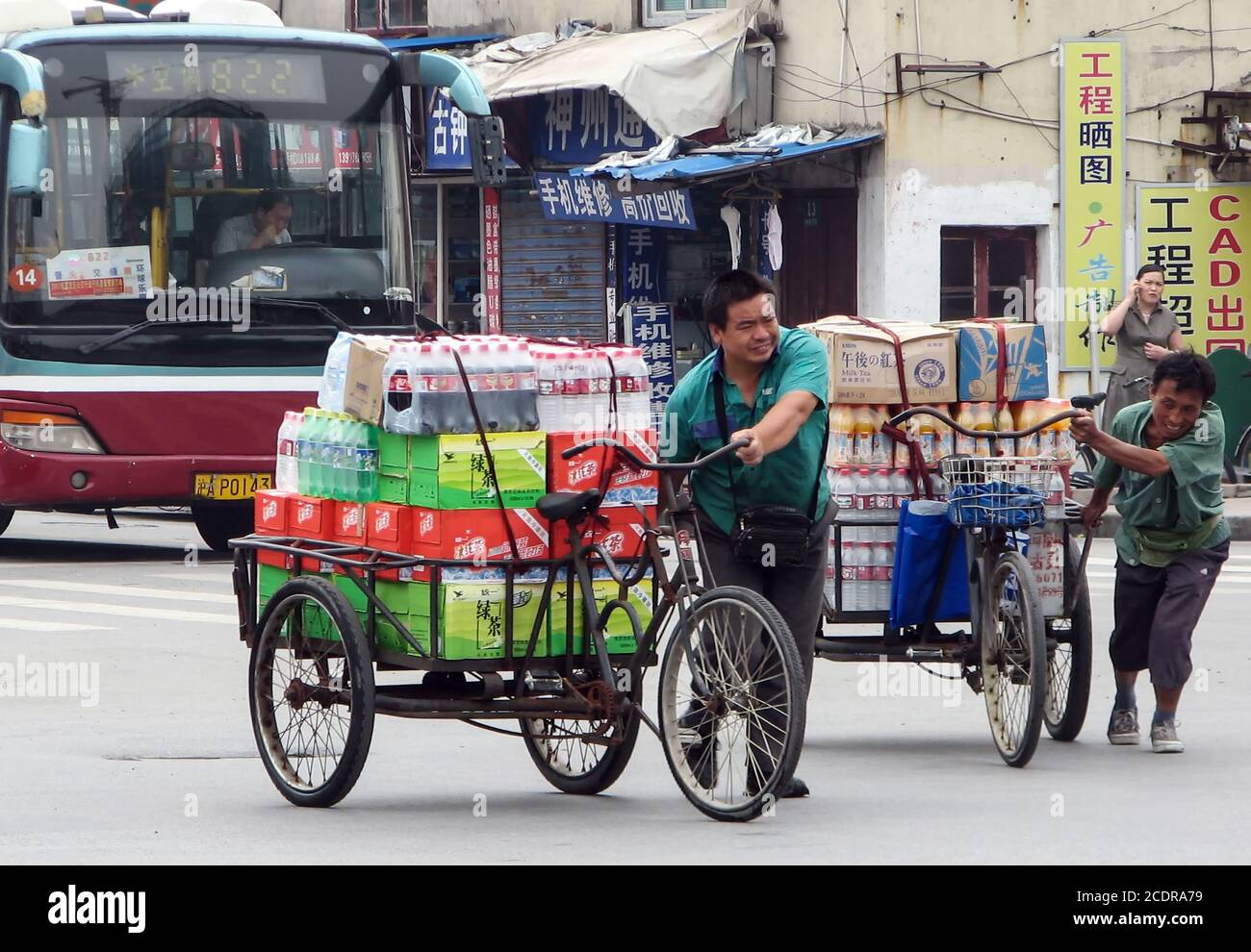 Schweres Gehen. Delivery Männer überqueren Hanzhong Road, Shanghai, während ein Busfahrer es schafft, mit Essstäbchen zu fahren und zu essen! Stockfoto