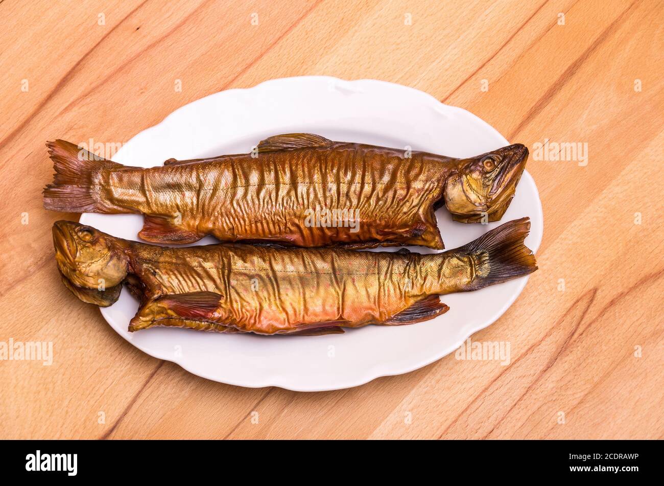 Zwei geräucherte Fische, Bachforelle, auf einem weißen Teller auf einem Buchentisch. Stockfoto