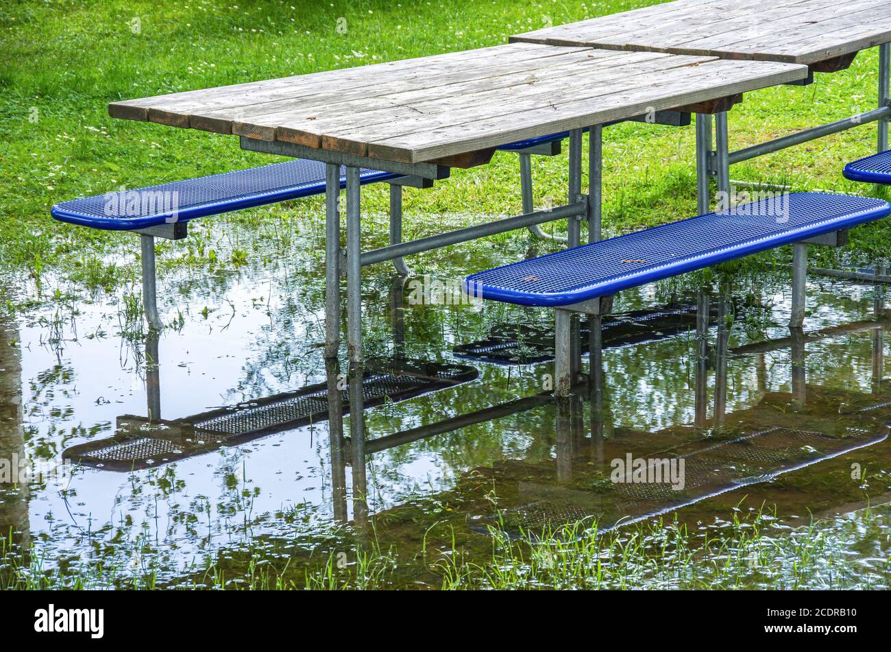 Tische und Bänke auf einem überfluteten Wiesengrund nach Hochwasser. Stockfoto