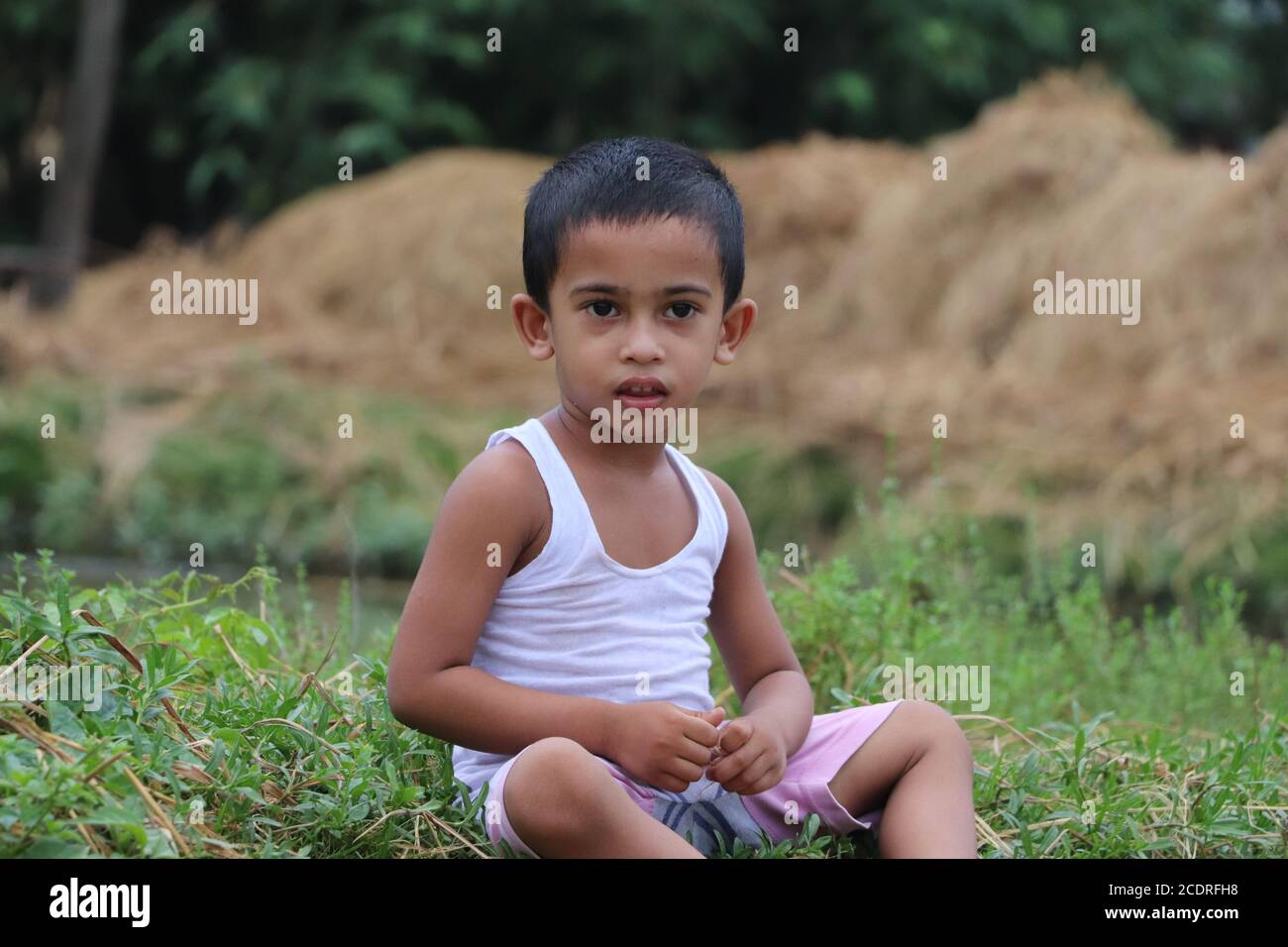Drei Jahre alt nachdenkliche asiatische Kind sitzt neben einem See Und die Kamera betrachten Stockfoto