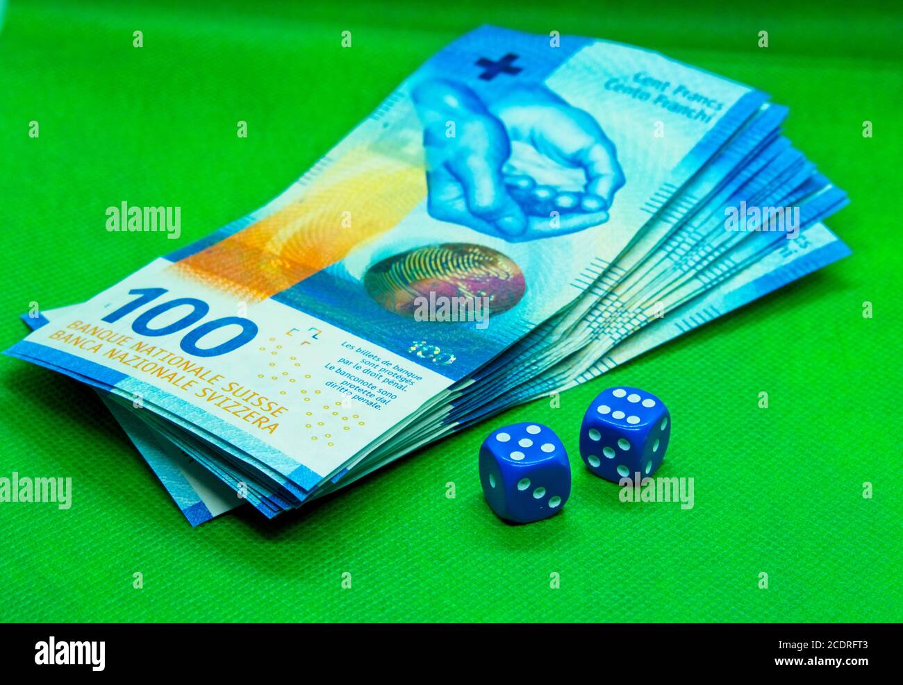 Zwei blaue Würfel neben Schweizer Franken-Scheinen mit einem Grüner Hintergrund Stockfoto