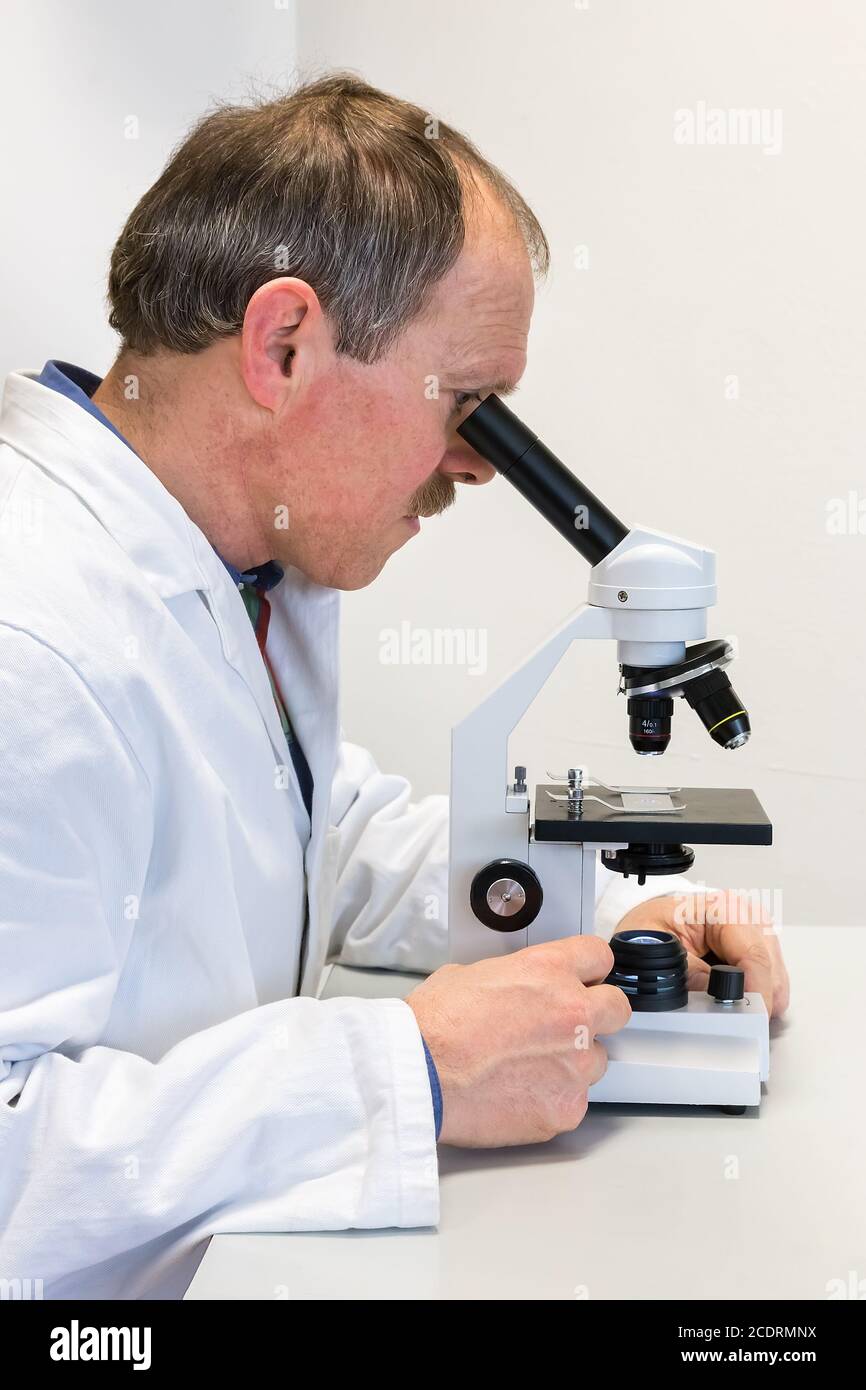 Biologe im Labormantel, der durch das Mikroskop schaut Stockfoto