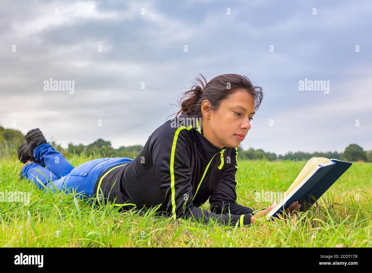 Junge Frau liegt im Gras Buch lesen Stockfoto