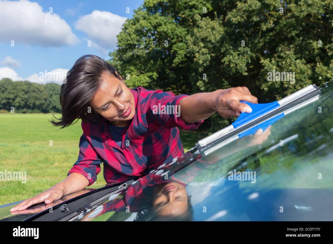 Junge Frau Reinigung Auto Windschutzscheibe in der Natur Stockfoto