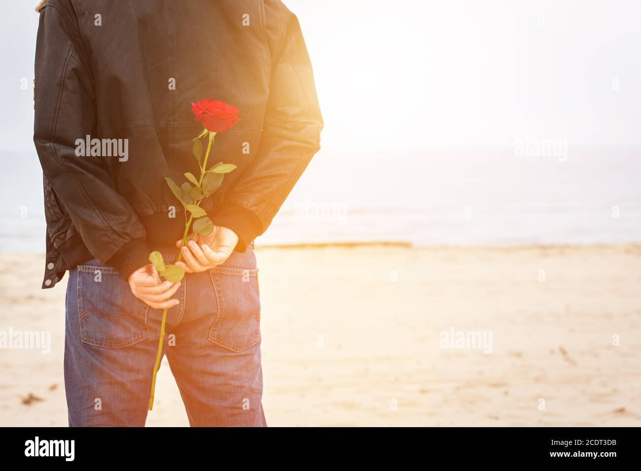 Mann mit einer Rose hinter seinem Rücken wartet auf Liebe. Romantisches Date am Strand Stockfoto