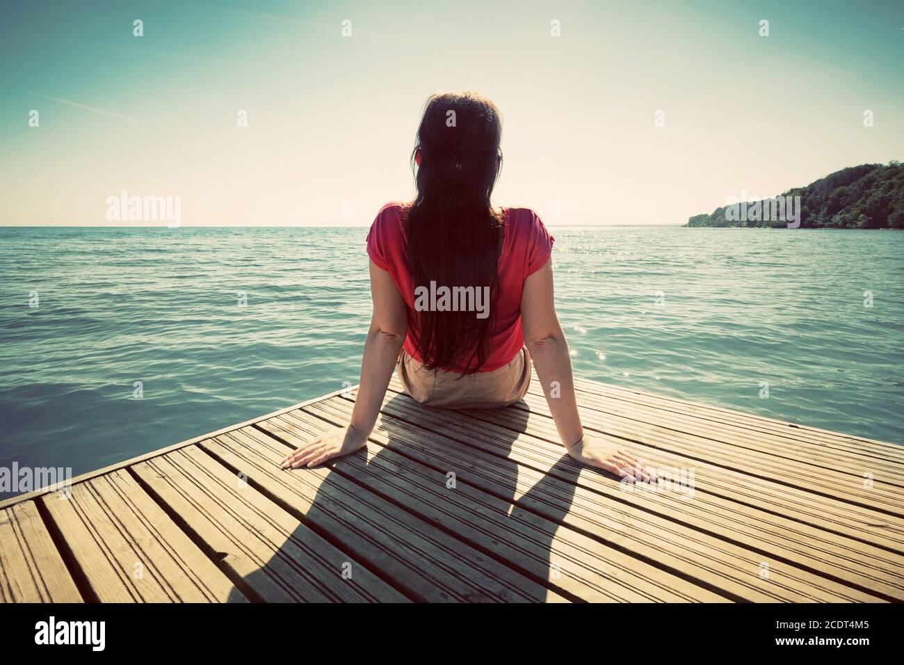 Junge Frau, die sich am Steg ausruhte und am sonnigen Sommertag das ruhige Meer betrat. Stockfoto
