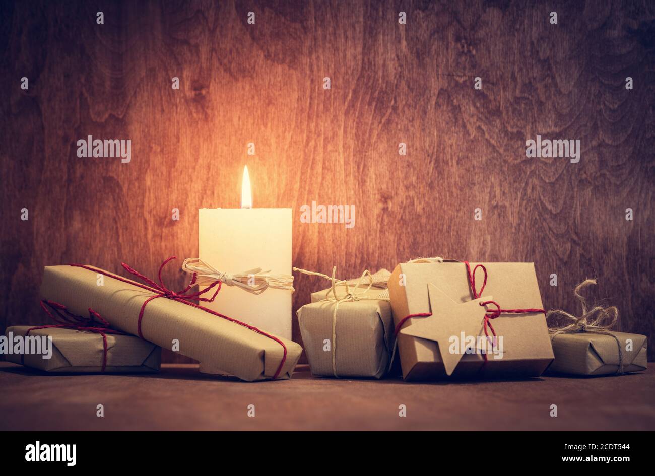 Weihnachtsgeschenke, Geschenke mit einer Kerze, die auf Holzwand Hintergrund leuchtet. Stockfoto