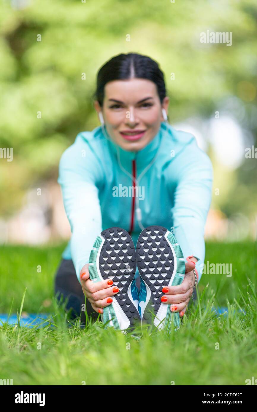 Frau erwärmt Muskeln vor dem Joggen. Sitzen auf Gras im Stadtpark - Frau dehnende Muskeln. Konzentrieren Sie sich auf die Füße. Stockfoto