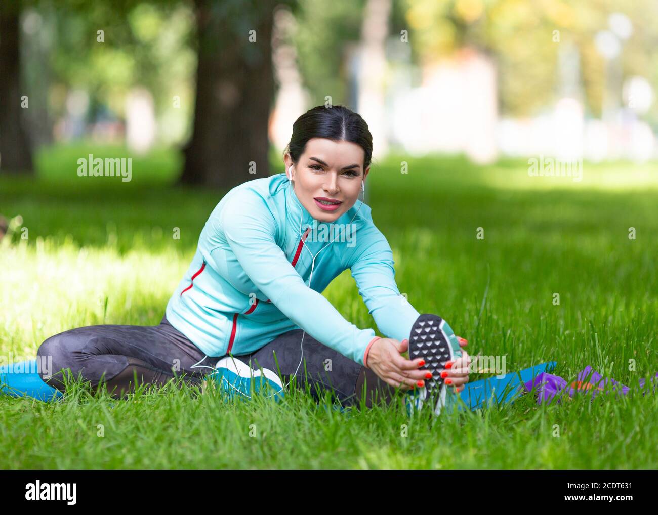 Frau erwärmt Muskeln vor dem Joggen. Sitzen auf Gras im Stadtpark - Frau dehnende Muskeln. Stockfoto