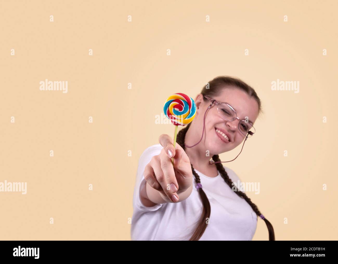 Lächelndes Mädchen hält einen Lutscher. Süßigkeiten Tag. Das Mädchen ist gut gelaunt. Farbige Lollipop für Süßigkeiten Tag. Das fröhliche Mädchen wird gegen ein gelbes b geschossen Stockfoto