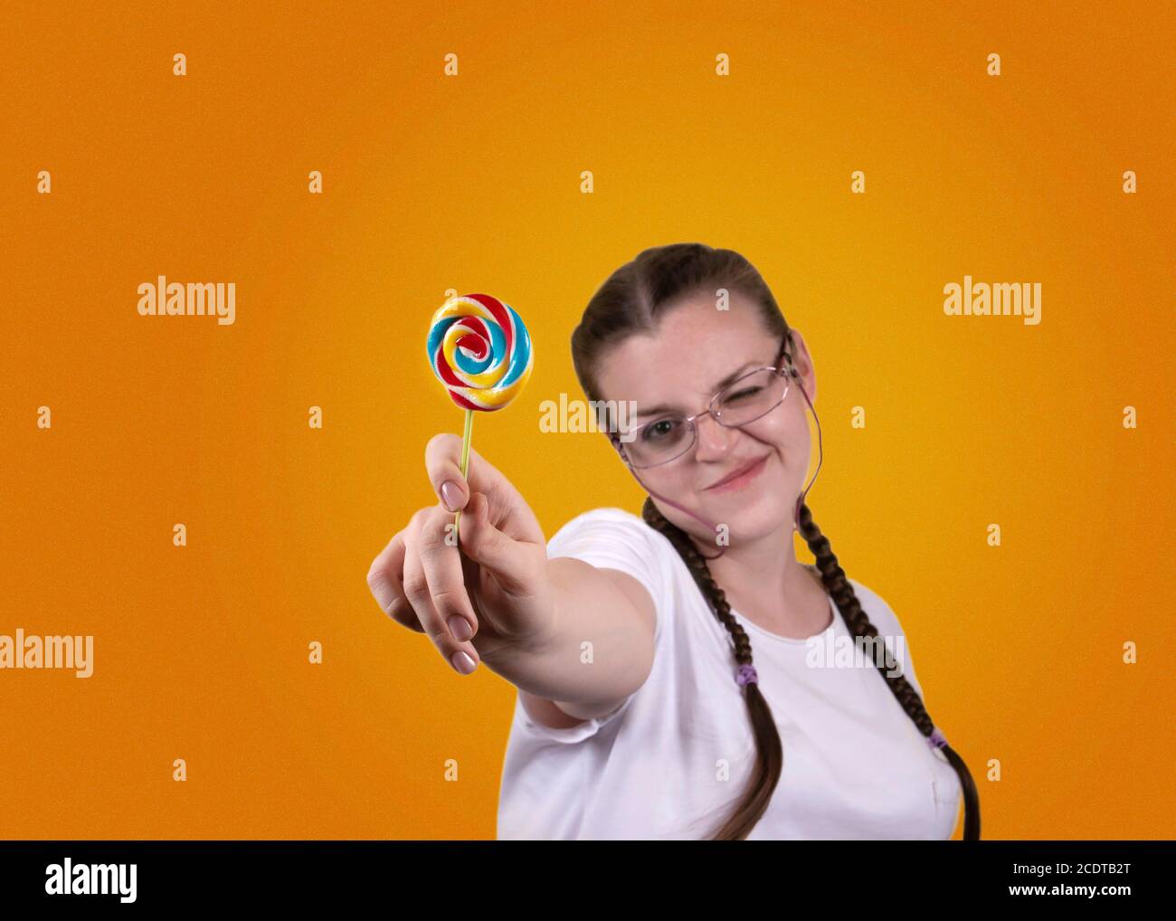 Lächelndes Mädchen hält einen Lutscher. Süßigkeiten Tag. Das Mädchen ist gut gelaunt. Farbige Lollipop für Süßigkeiten Tag. Das fröhliche Mädchen wird gegen ein gelbes b geschossen Stockfoto