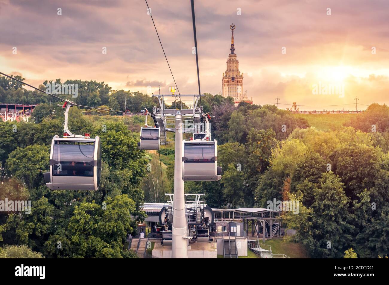 Seilbahn auf Sparrow Hills bei Sonnenuntergang, Moskau, Russland. Die Kabinen der Seilbahn bewegen sich über den Park, das Hauptgebäude der Moskauer Staatlichen Universität in der Ferne. Wunderschön Stockfoto