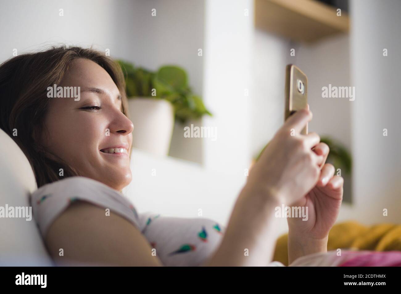 Junge Frau mit Handy zu Hause lächelnd Stockfoto
