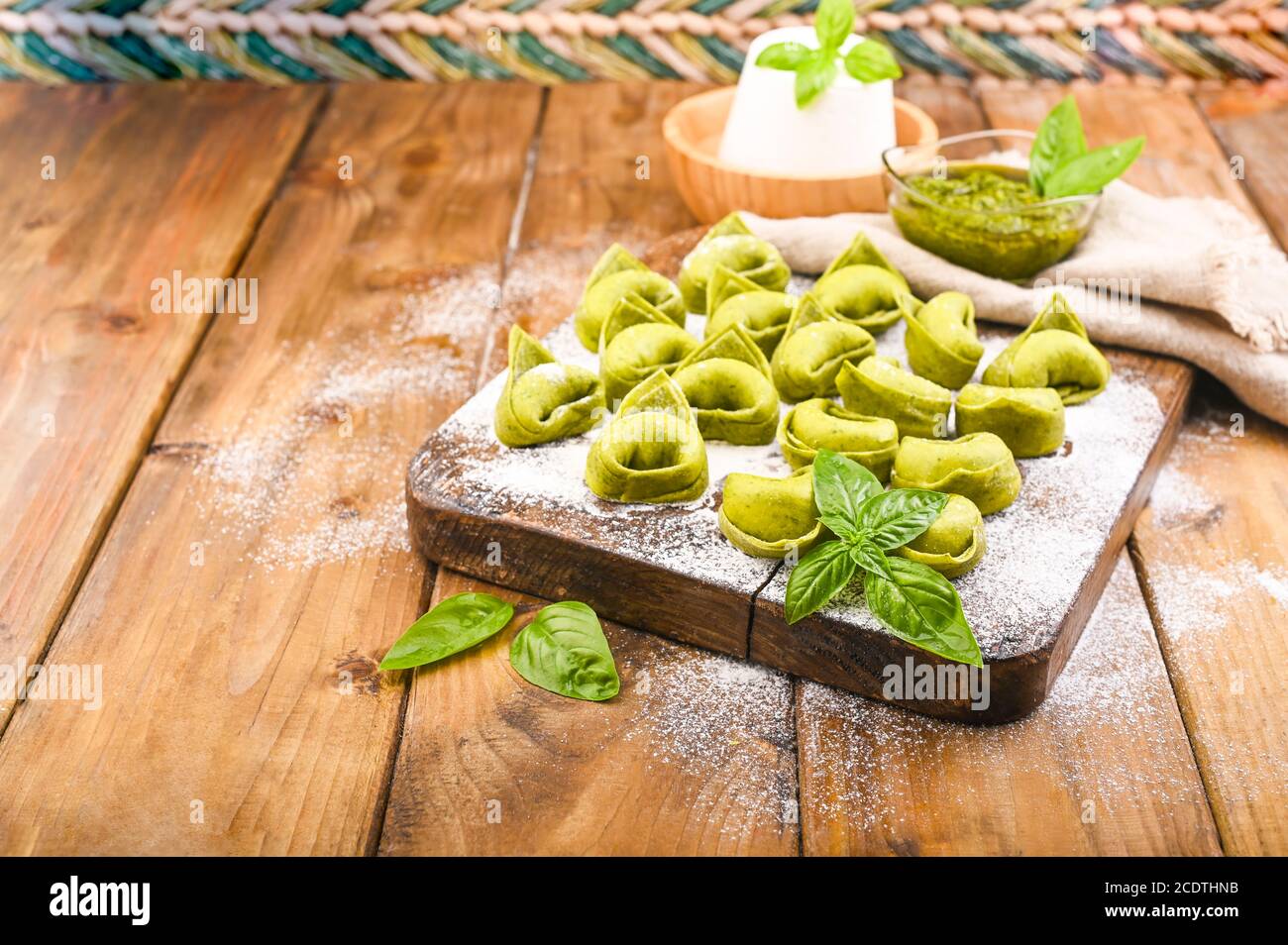 Tortellini e Tortelloni typische Gerichte emilia italien. Food Hintergrund mit hausgemachten rohen italienischen Tortelloni und Zutaten für grünes Pesto auf Holzhintergrund . Weitwinkelansicht. Speicherplatz kopieren. Stockfoto