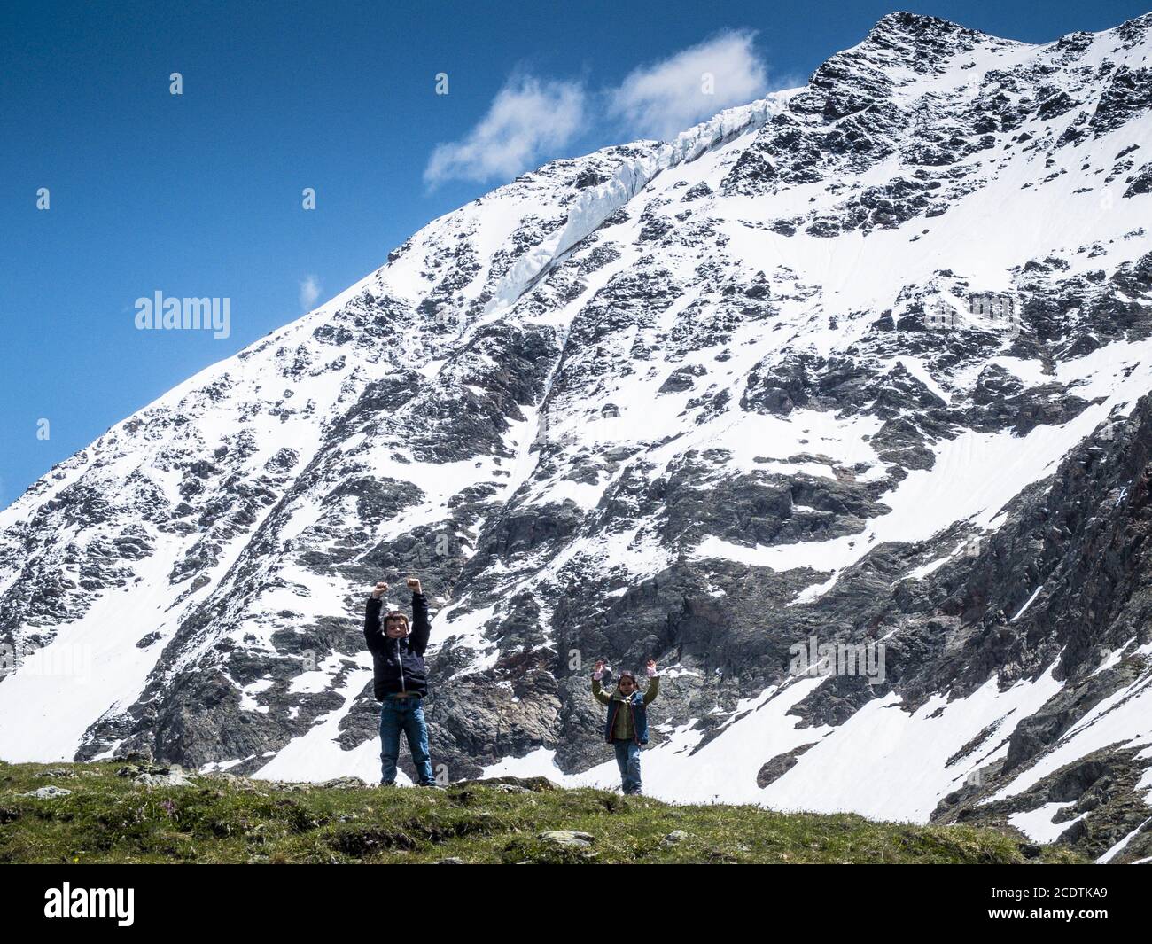 Kinder auf einem Berg heben ihre Hände zum Himmel, auf dem Berghintergrund mit Schnee Stockfoto